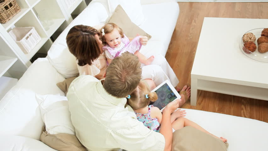 Young Caucasian couple home couch cute daughters wireless tablet
