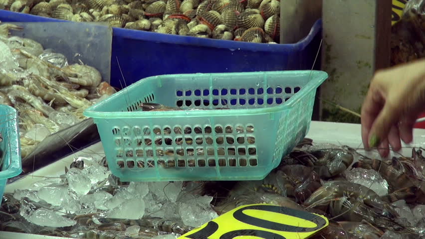 woman buying shrimps / woman is picking up shrimps in a street market and putting them in the shopping basket, woman hand's close-up