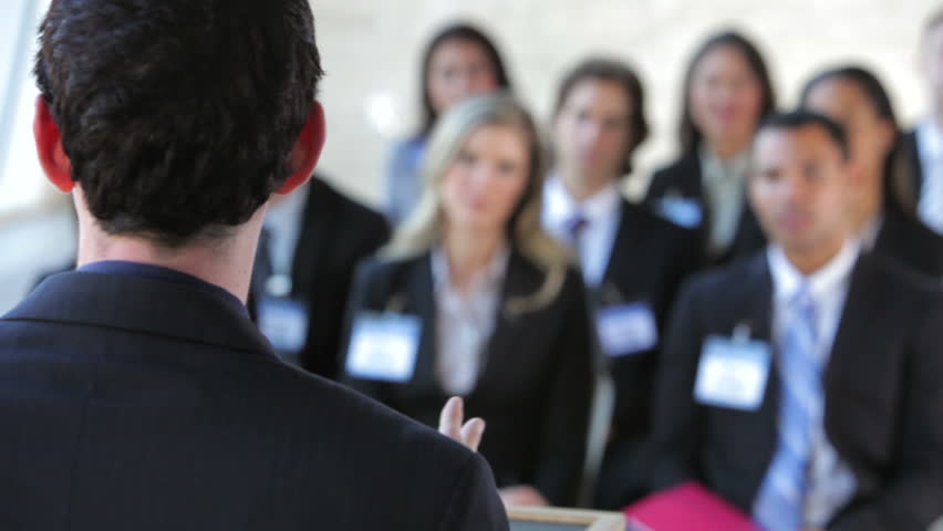 Focus pulled fro businessman addressing conference to female delegate raiseing her hand to ask a question. Shot on Canon 5d Mk2 with a frame rate of 30fps