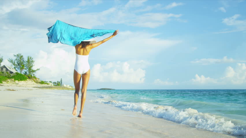 Beautiful carefree girl white swimsuit celebrating achieving her beach lifestyle by blue ocean waters shot on RED EPIC