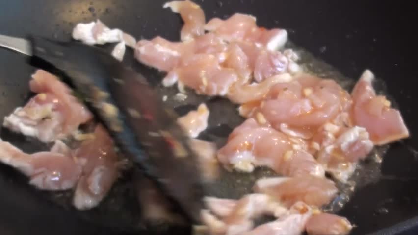 Stewing pieces of chicken in frying pan, stirring, close up