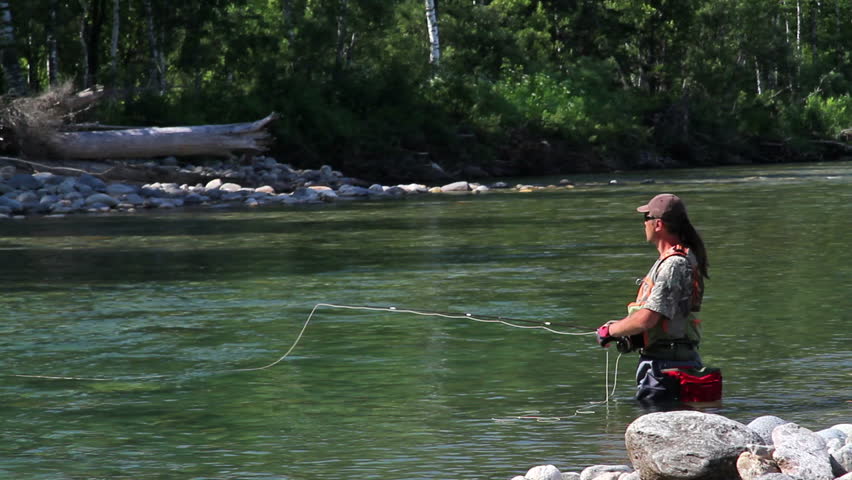 Fly fishing for trout fishing. Man in a professional fishing gear is in the water and fishing on fly fishing