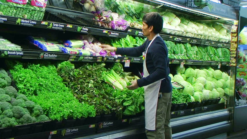 Worker facing  fresh vegetables in grocery store. 