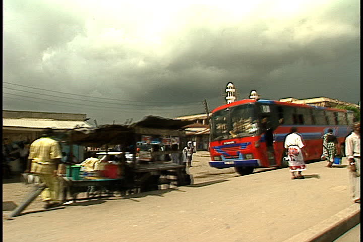 DAR ES SALAAM, TANZANIA - DECEMBER 1, 1998: Tracking shot from moving car past many pedestrians, parked cars and buildings.