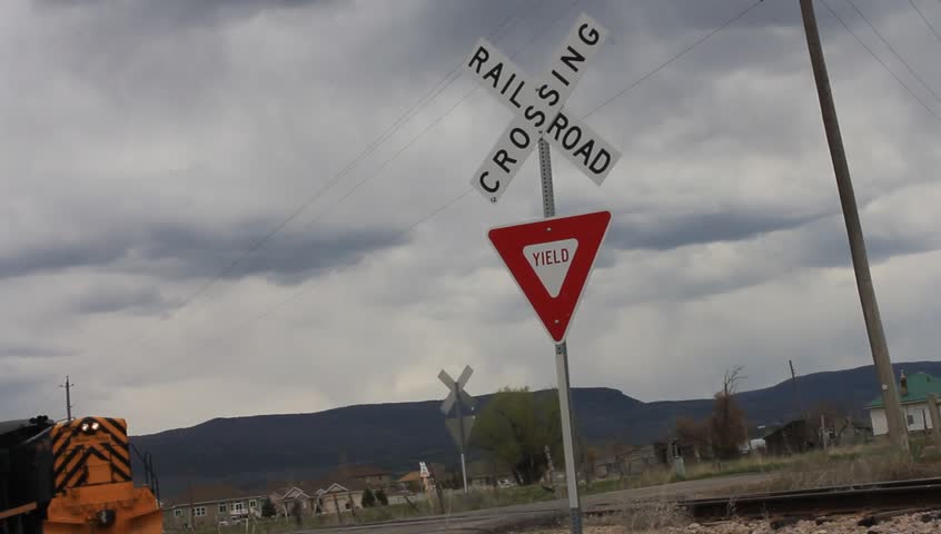 A rail road crossing and yield sign, as a train passes.