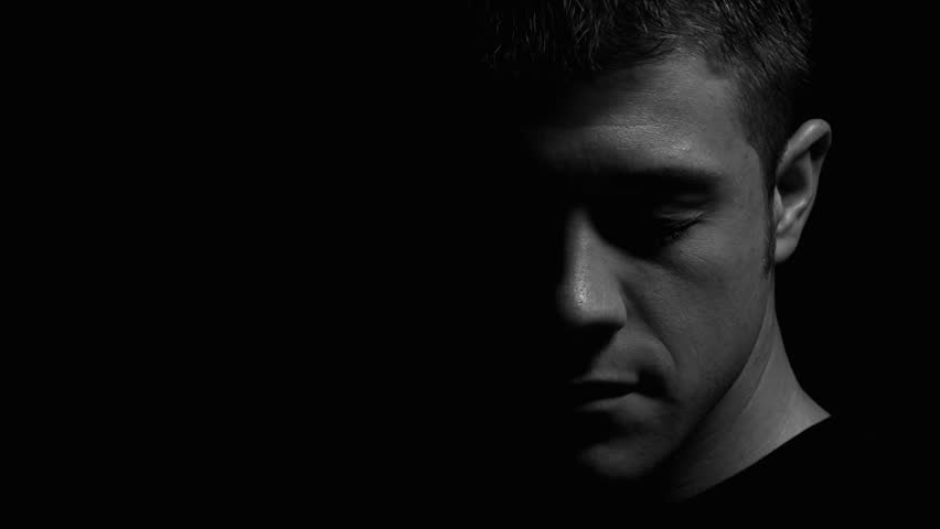 Man facing down with eyes closed in black and white. Experimental lighting. 