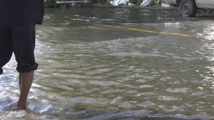 Bangkok, Thailand - October 2011: A bottle floats down a flooded road and is picked up by a barefooted man with his trousers rolled up.