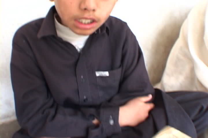 PESHAWAR, PAKISTAN - NOVEMBER 01, 2001: Close up of open pages of Koran, camera tilts up to boy in Muslim dress rocking back and forth.