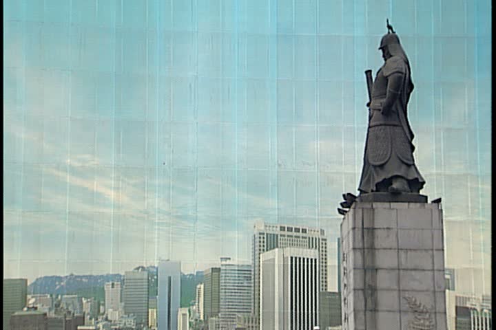 SEOUL - FEBRUARY 26, 1997: MS statue of Admiral Yi Sun Sin reflected on side of glass building. WS showing statue, building, and traffic passing on Sejong Avenue.