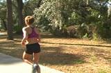 A beautiful young woman jogs away from the camera in a lovely natural setting on a sidewalk surrounded by trees.  The jib-mounted camera cranes up and to the left to follow.