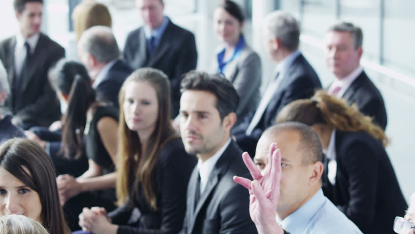 A multi ethnic group of business people of mixed ages are listening to a presentation at a business seminar and asking questions. 