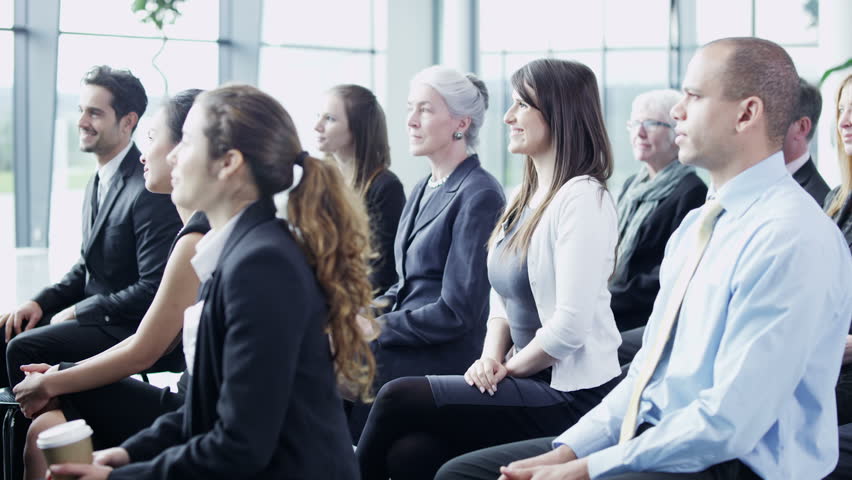 A multi ethnic group of business people of mixed ages are listening to a presentation at a business seminar and asking questions. 