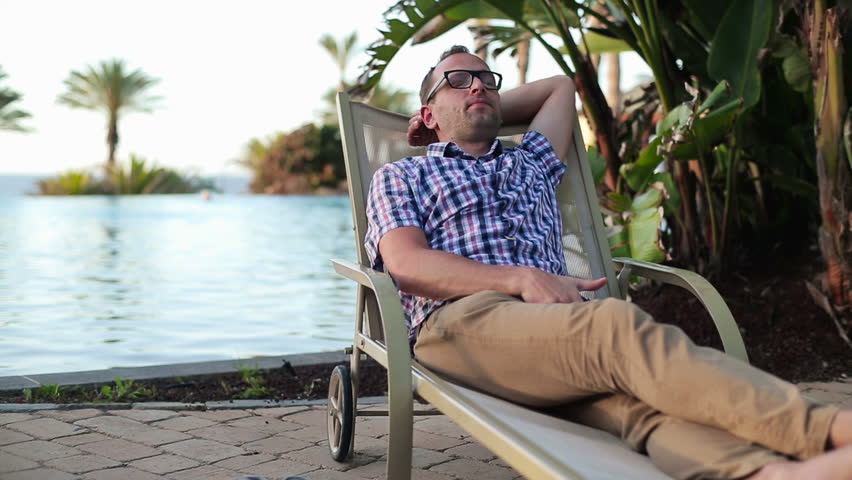 Young man on sunbed by the pool talking on cellphone
