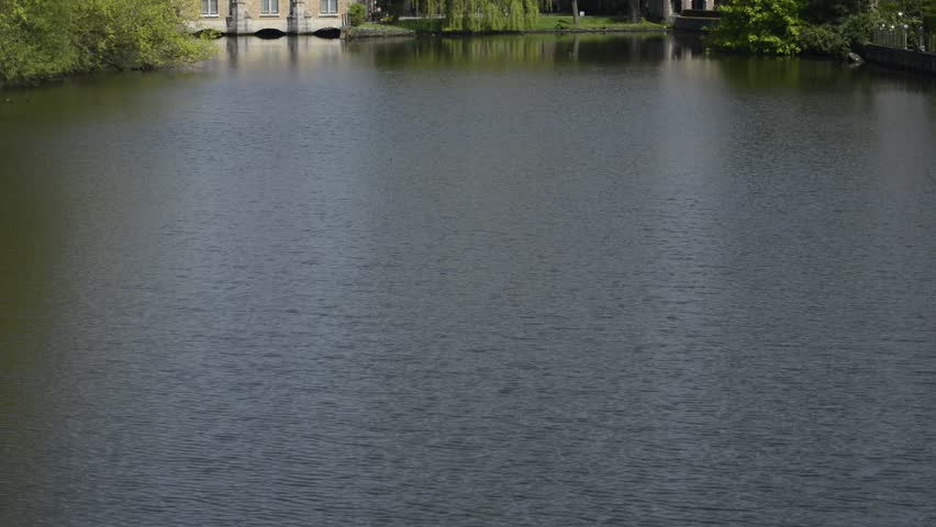 Minnewater lake (Lake of Love) in Bruges, Belgium: camera moves from bottom to top showing water then Sluice House (Sashuis) close to the water and Church of Our Lady
