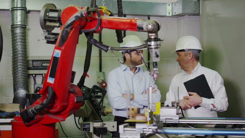 A mature male factory manager is with a young male client or colleague and is explaining how some of the plant machinery works. 