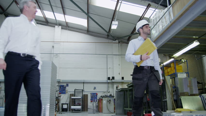 Happy and friendly team of workers in a warehouse or factory come together as they walk around the factory floor. They may be the owners of the business or part of the company team. In slow motion.