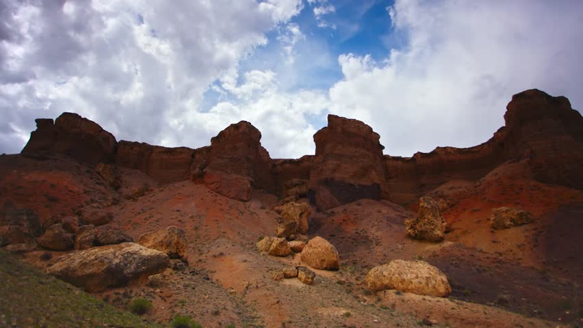 Timelapse over the Charyn (Timerlik) Canyon. Fluffy clouds above red rock mountain peak. Natural landscape erosion and grand canyons with stunning rock formations.
