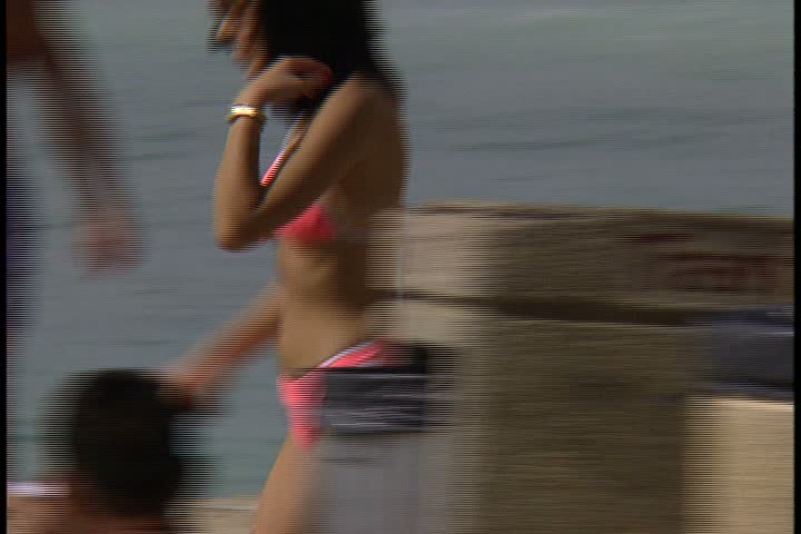 WAIKIKI BEACH, HONOLULU, HAWAII - JANUARY 30, 1997: scenic b-roll of Waikiki Beach, Hawaii: CU track woman in bright pink bikini, she walks on crowded beach then sits down on towel.