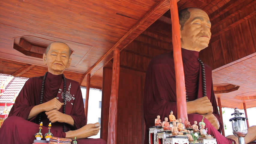 BANGKOK, THAILAND, 2013: Two oversized Buddhist monk statues sit amongst several smaller statues at a temple in Bangkok, Thailand.