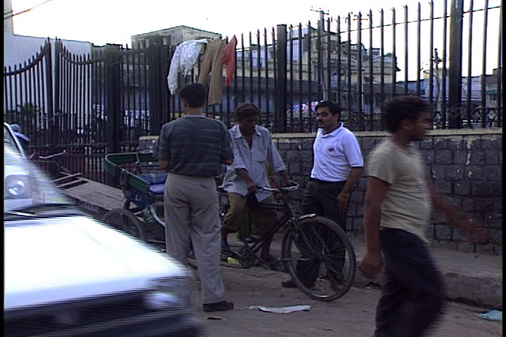 DELHI, INDIA - JULY 28, 1999: Tightly framed shot of passing cars, bicycles, motor bikes, pedestrians and merchants pushing carts.