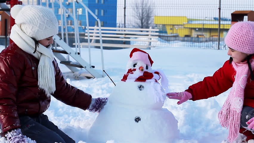 Happy girls playing with snowman in park