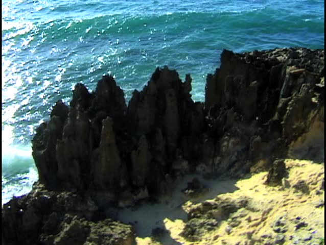 Jagged lava stone formations are pounded by surf in this low perspective aerial footage.