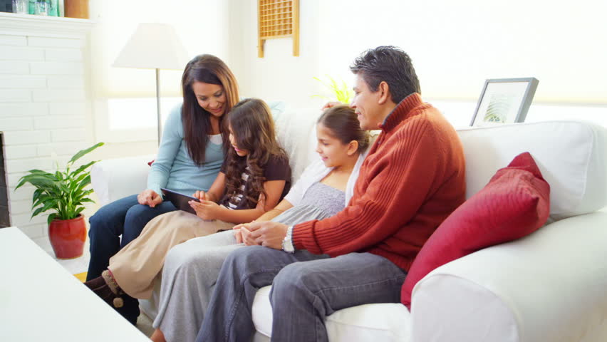 A mom and sister join their family on the couch to play with a tablet computer. Wide shots.
