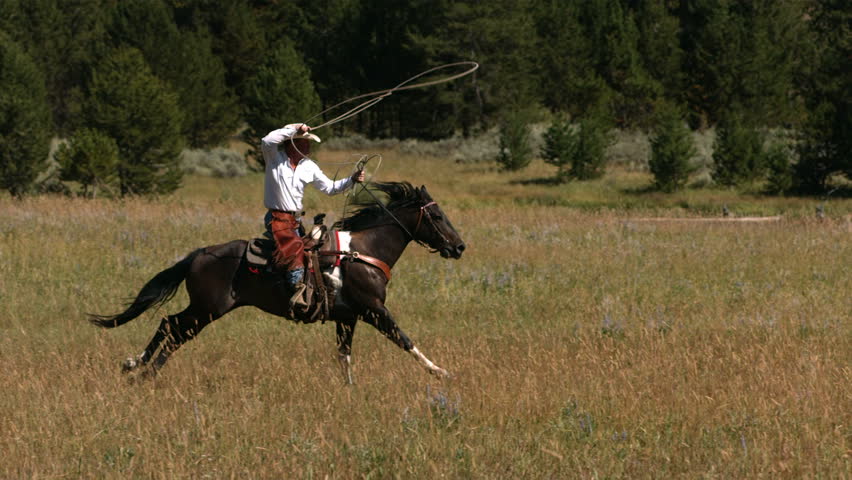 Cowboy on galloping horse swings lasso, slow motion