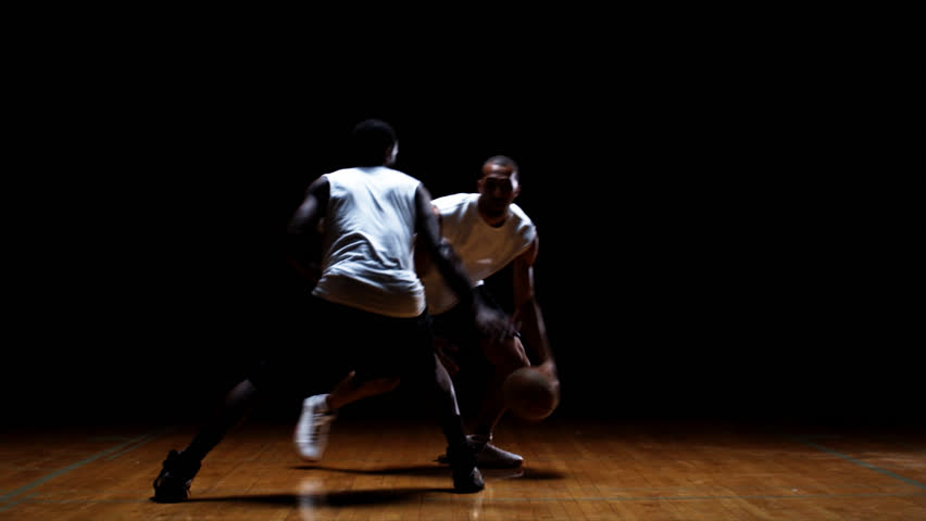 A basketball player does tricks with the ball in front of the defender and makes him jump around 
