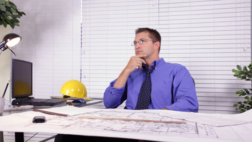 A young architect, builder, or designer going over a set of house plans he is working on, stops and smiles at the camera. Jib footage.