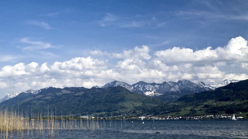 A moving postcard: Reed, clouds, snowy mountains and a lake in time-lapse