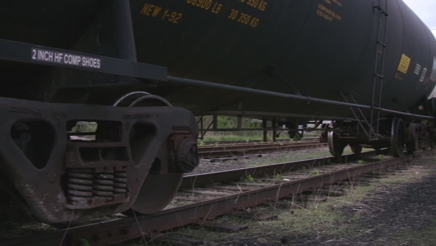 A pan along the tracks at wheel level, showing 3 tankers and traffic crossing in the distance.