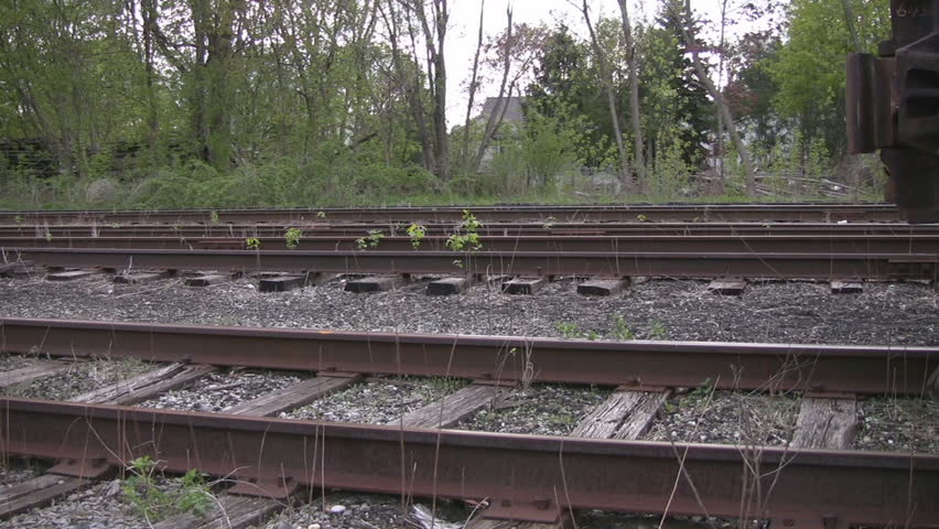 A pan along the tracks, ultimately getting to the first set of wheels on a rail car, with the portion of a ladder visible.