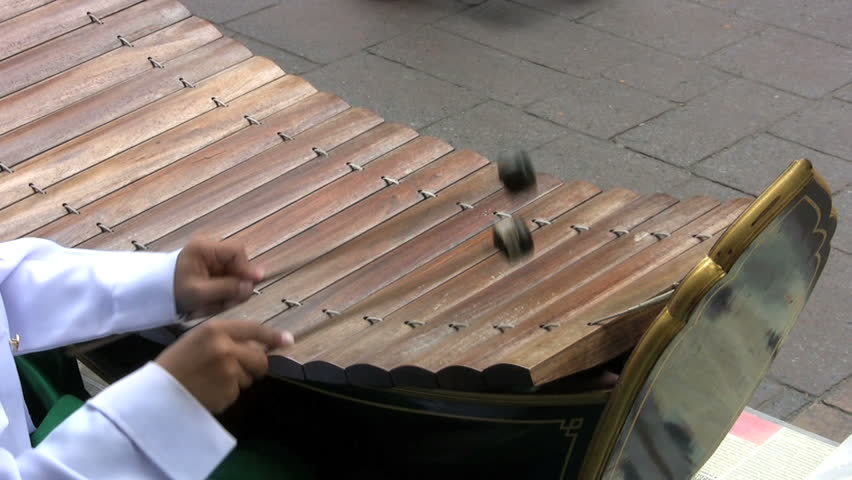 A young Thai boy plays a wooden xylophone outside near the market trying to generate some income.