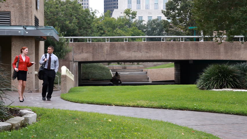 Two business people or coworkers engaged in conversation walking through an urban park.
