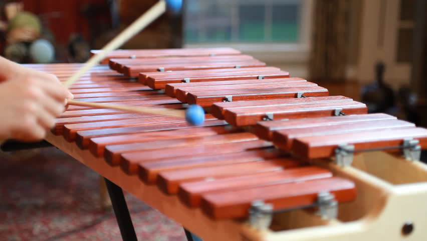 Close up of a boy using blue tipped mallets to play a tune on a marimba.