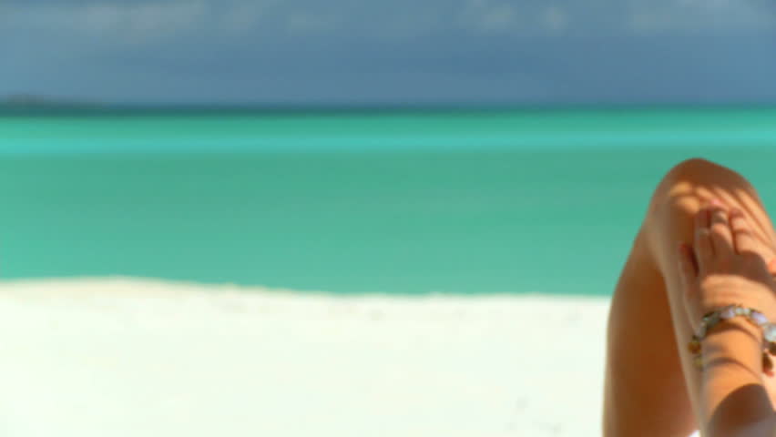 Elegant young female relaxing on white sandy beach looking at aquamarine waters