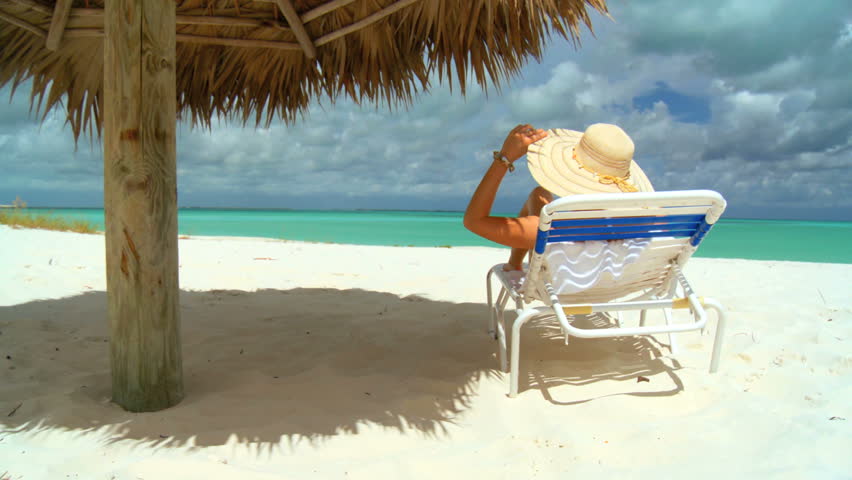 Elegant young female relaxing on white sandy beach looking at aquamarine waters