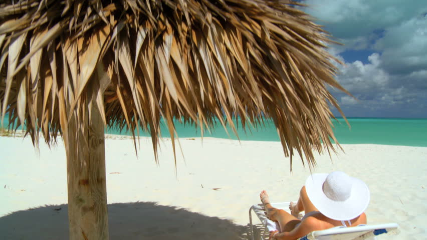 Elegant young female relaxing on white sandy beach looking at aquamarine waters