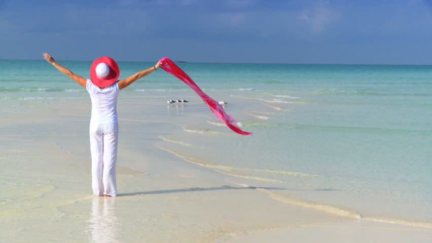Elegant young female celebrating on a beautiful white sandy beach looking at aquamarine waters 60 FPS