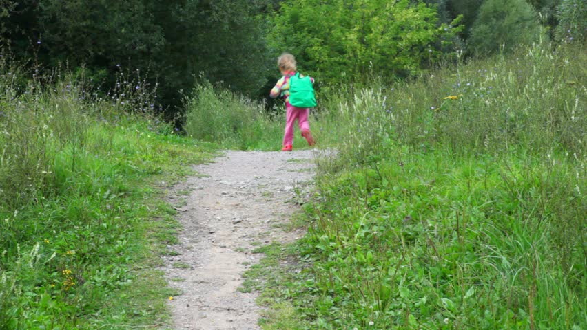 little girl with rucksack running in park from camera 