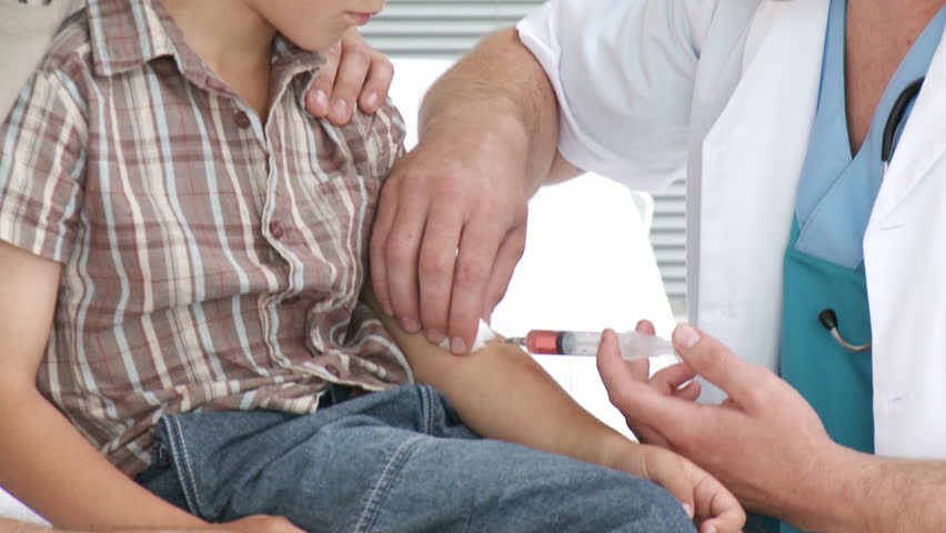 Footage in high definition of attractive male doctor giving a little boy an injection in hospital