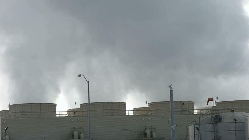 Pollution and steam spewing from cooling towers and smoke stacks of a natural gas electrical generating power plant. White and grey smoke with a while background sky.