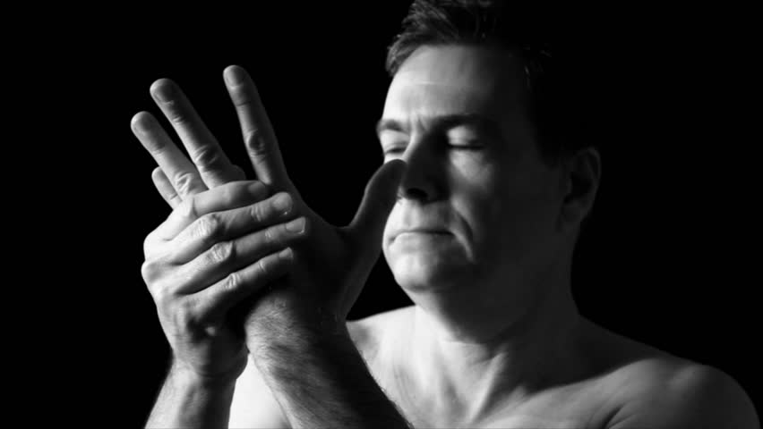 A man who is holding his wrist as if in pain from an injury or from arthritis in his joints.