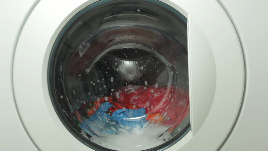 A front-loading washing machine filled with brightly colored tumbling clothing; includes ambient sound.