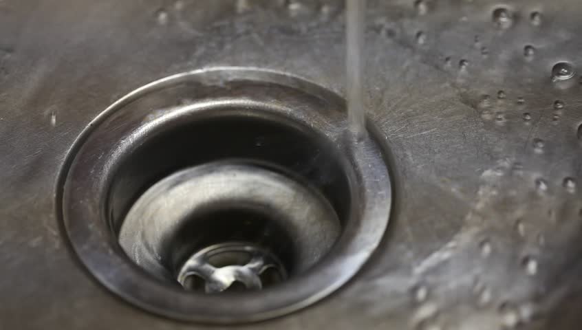 Water running down into stainless steel sink and into drain. Short depth of field and medium flow