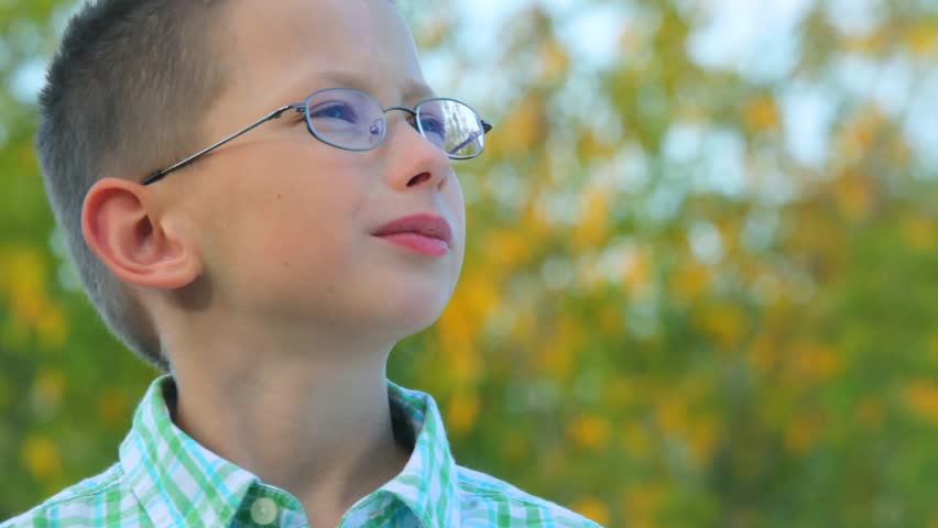 portrait of bespectacled boy stands against trees in park 
