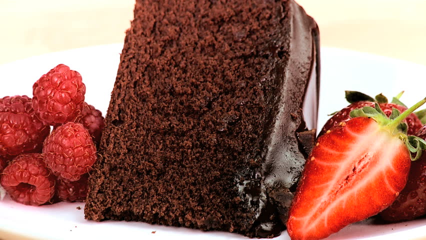 Indulgent chocolate cake & strawberries being covered in sweet sticky sauce on white background