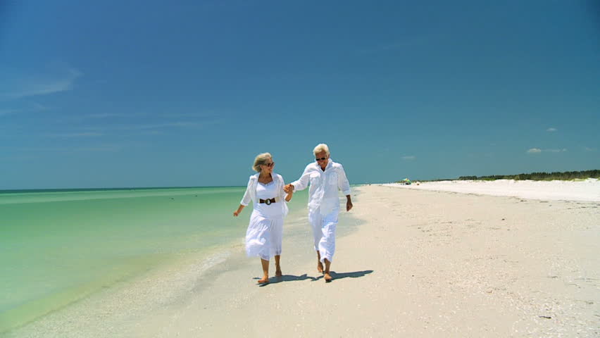 Attractive senior carefree couple running along the beach barefoot enjoying a fun lifestyle 60FPS