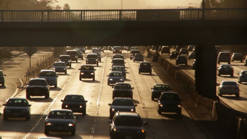 Heavy traffic on the Hollywood Freeway in Los Angeles at rush hour, beneath the setting sun and an overpass in an urban setting.